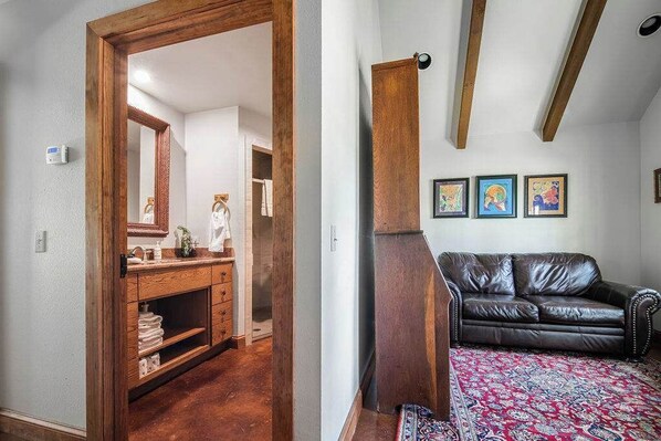 Ein Zimmer mit Holztür zu einem Badezimmer, einem schwarzen Ledersofa und einem gemusterten Teppich.