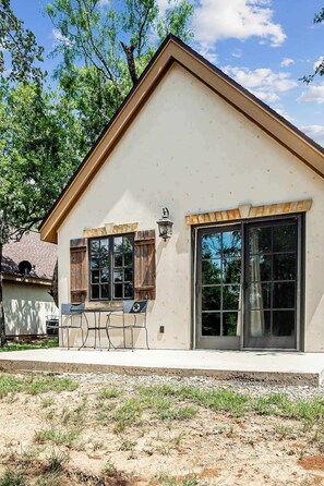 Einbungalow mit hellbeige Fassade, großen Fenstern und einer Terrasse mit einem Metalltisch und Stühlen.