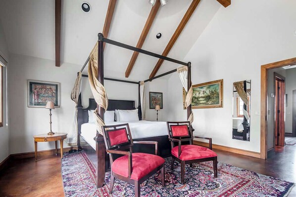 A four-poster canopy bed with a red upholstered chair and a small table beside it.