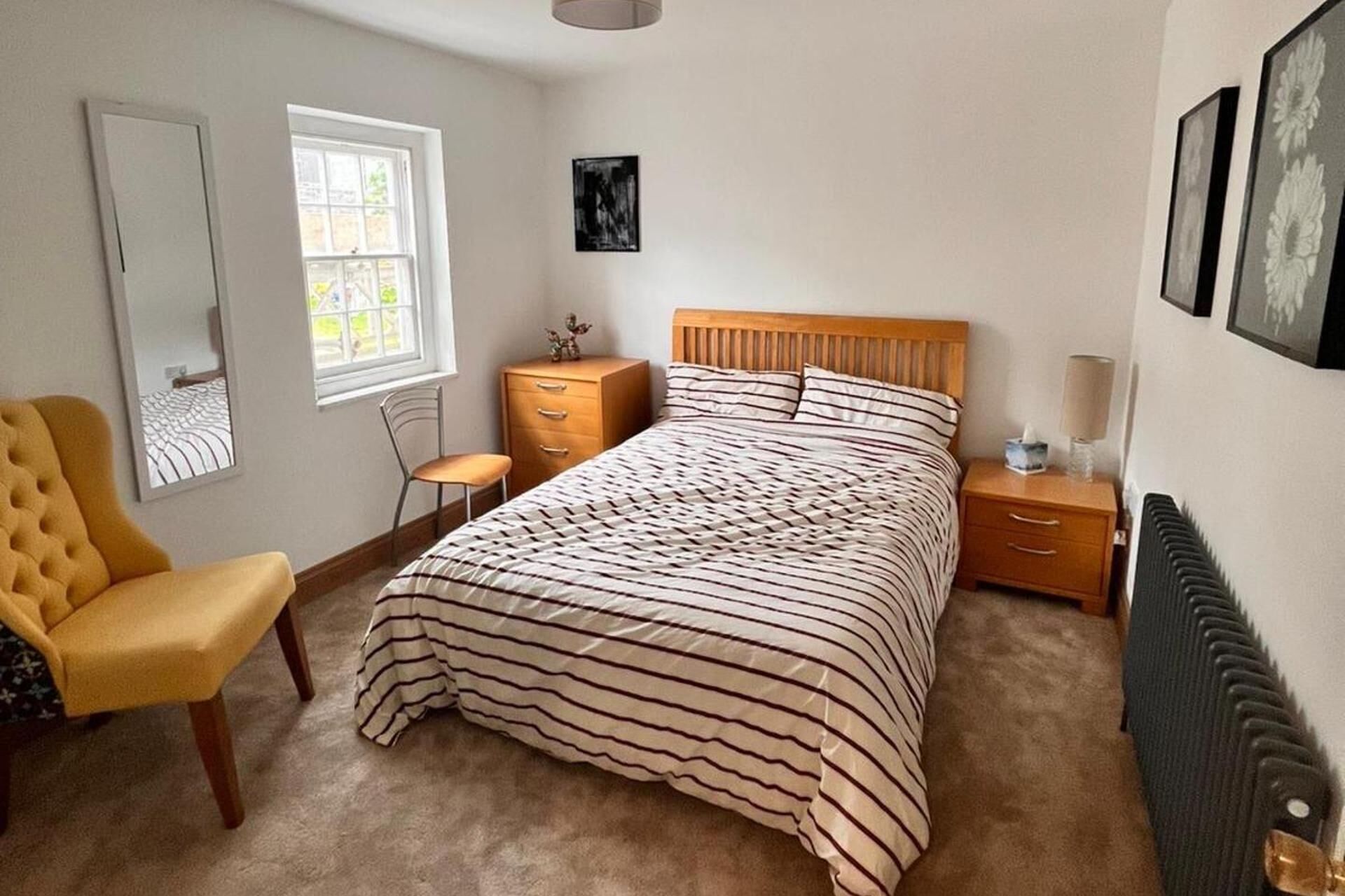 A bedroom with a bed, a chair, a dresser, a nightstand, and a radiator.