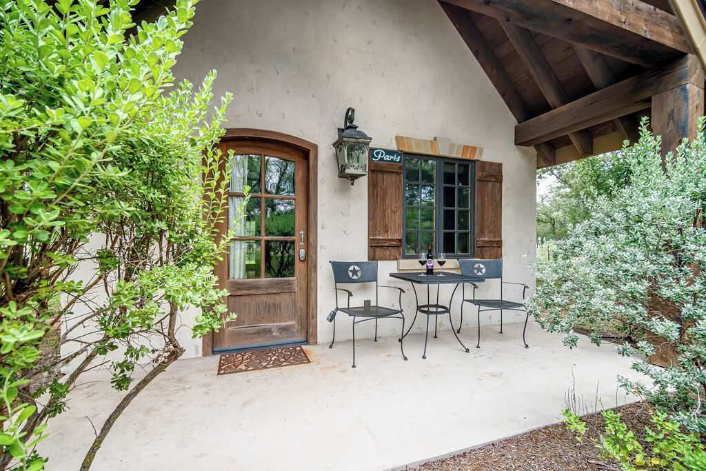 A rustic building with a wooden door, a window with shutters, and a table with chairs outside.