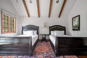 A room with two wooden beds, a patterned carpet, a table with a lamp, and a 'PARIS' framed picture on the wall. - The Manor Haus at Messina Hof Hill Country Winery-Paris Haus (Fredericksburg)
