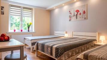 Un dormitorio con dos camas, una ventana con persianas, una mesa con fruta y un cuadro en la pared.