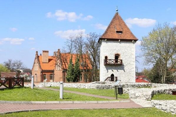 A historic stone tower with a conical roof, surrounded by a stone wall and a grassy area with a paved path.