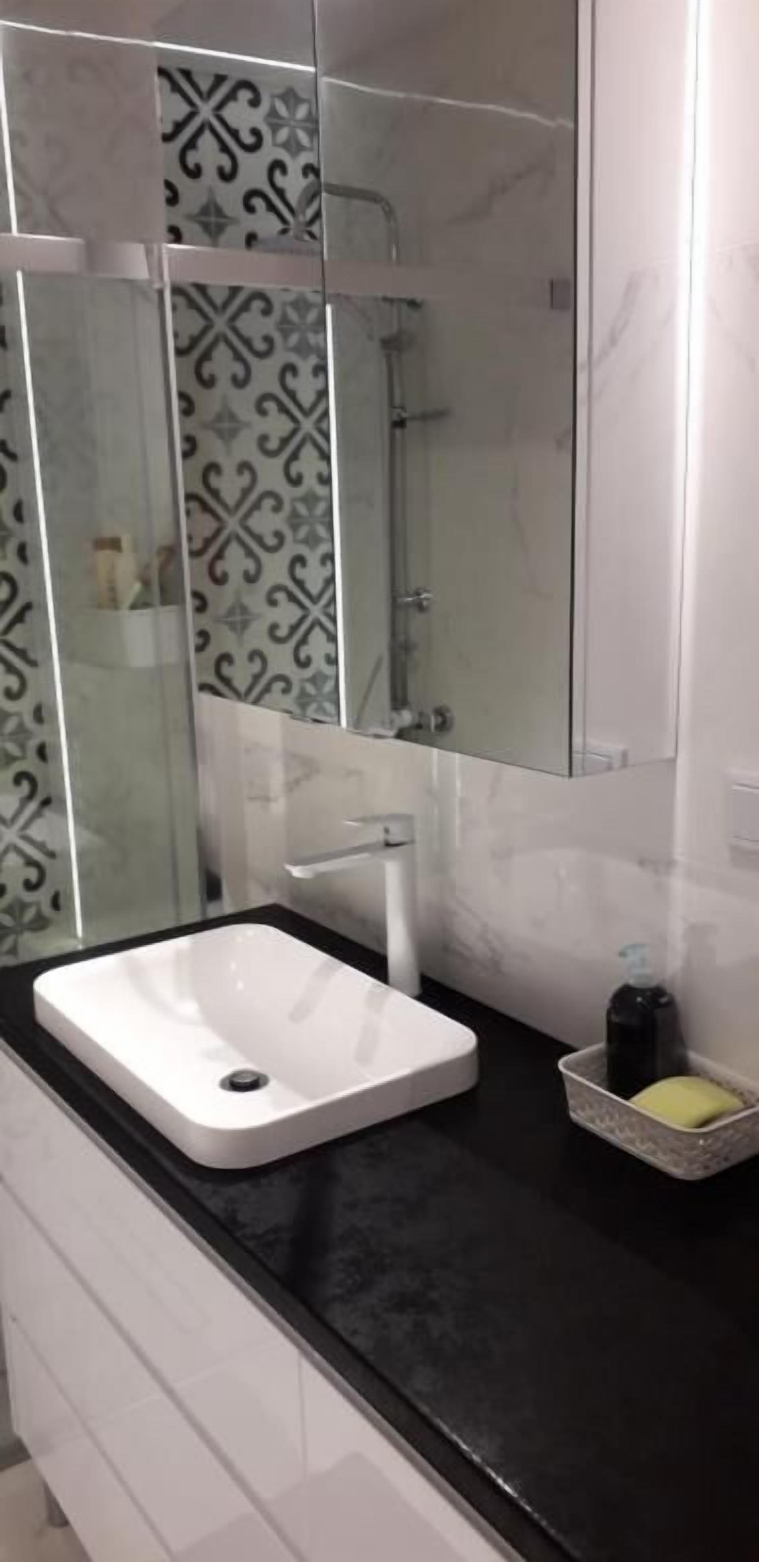 Un baño moderno con un lavamanos blanco, encimera negra y azulejos estampados.