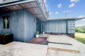 Ein modernes Gebäude mit grauer Fassade, flachem Dach und einer Beton-Terrasse mit Topfpflanzen.