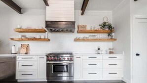 A modern kitchen with white cabinetry, a stainless steel stove, and wooden shelves above. - Unique Luxury Home-Near Alamo Springs Cafe (Fredericksburg)