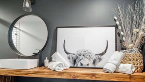 A bathroom vanity with a round mirror, a framed picture of a bull, and towels. - Unique Luxury Home-Near Alamo Springs Cafe (Fredericksburg)