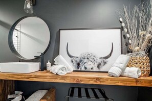 A bathroom vanity with a round mirror, a framed picture of a bull, and towels.