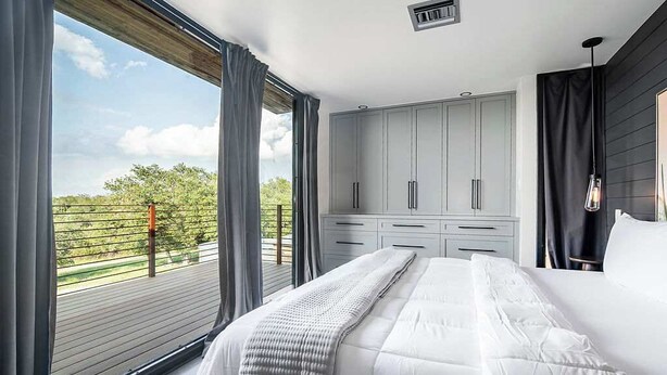 A bedroom with a large bed, a wardrobe, and a view of a deck and greenery. - Unique Luxury Home-Near Alamo Springs Cafe (Fredericksburg)