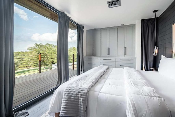 A bedroom with a large bed, grey cabinets, and a view of greenery outside.