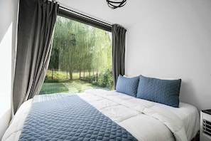 A bedroom with a large bed, grey curtains, and a view of a garden.