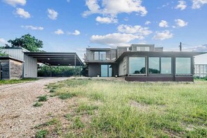 A modern house with a covered patio, large windows, and a gravel driveway.
