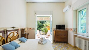 Une chambre d’hôtel avec un lit, une commode, un téléviseur et une vue sur le jardin, accessible par une porte ouverte.