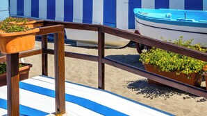 Une terrasse au bord de la plage, avec un mur rayé de bleu et de blanc, un bateau et une vue sur un château perché sur une colline.