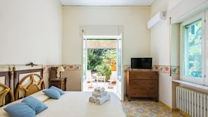 Habitación de hotel con cama, cómoda, televisión y vista al jardín por una puerta abierta.