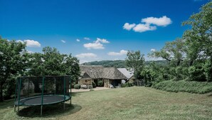 A stone house with a covered patio, surrounded by a grassy yard and trees.