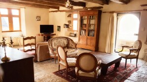 A cozy living room with a wooden ceiling, a television, a bookshelf, and a large window.