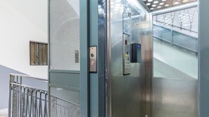 An elevator interior with a control panel, metallic walls, and a mesh door.