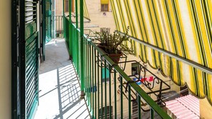 A narrow corridor with a tiled floor, green railings, and a striped awning.
