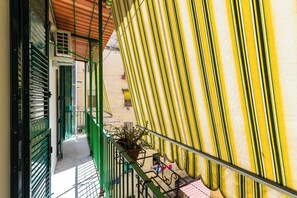 Un estrecho pasillo con contraventanas verdes, una planta en maceta y un toldo a rayas.