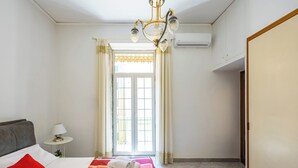 A hotel room with a bed, a nightstand, a lamp, a chandelier, and a window with curtains.