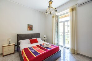 Una habitación de hotel con cama, mesita de noche, lámpara, ventana con cortinas y candelabro.