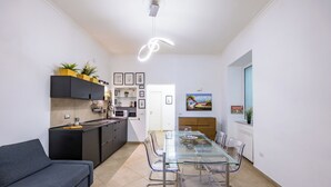 A modern kitchen with a glass dining table, grey sofa, and black cabinets.