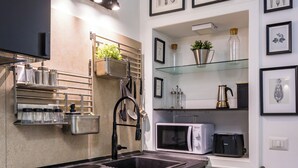 A modern kitchen with a black countertop, stainless steel appliances, and a glass shelf unit with kitchen utensils.
