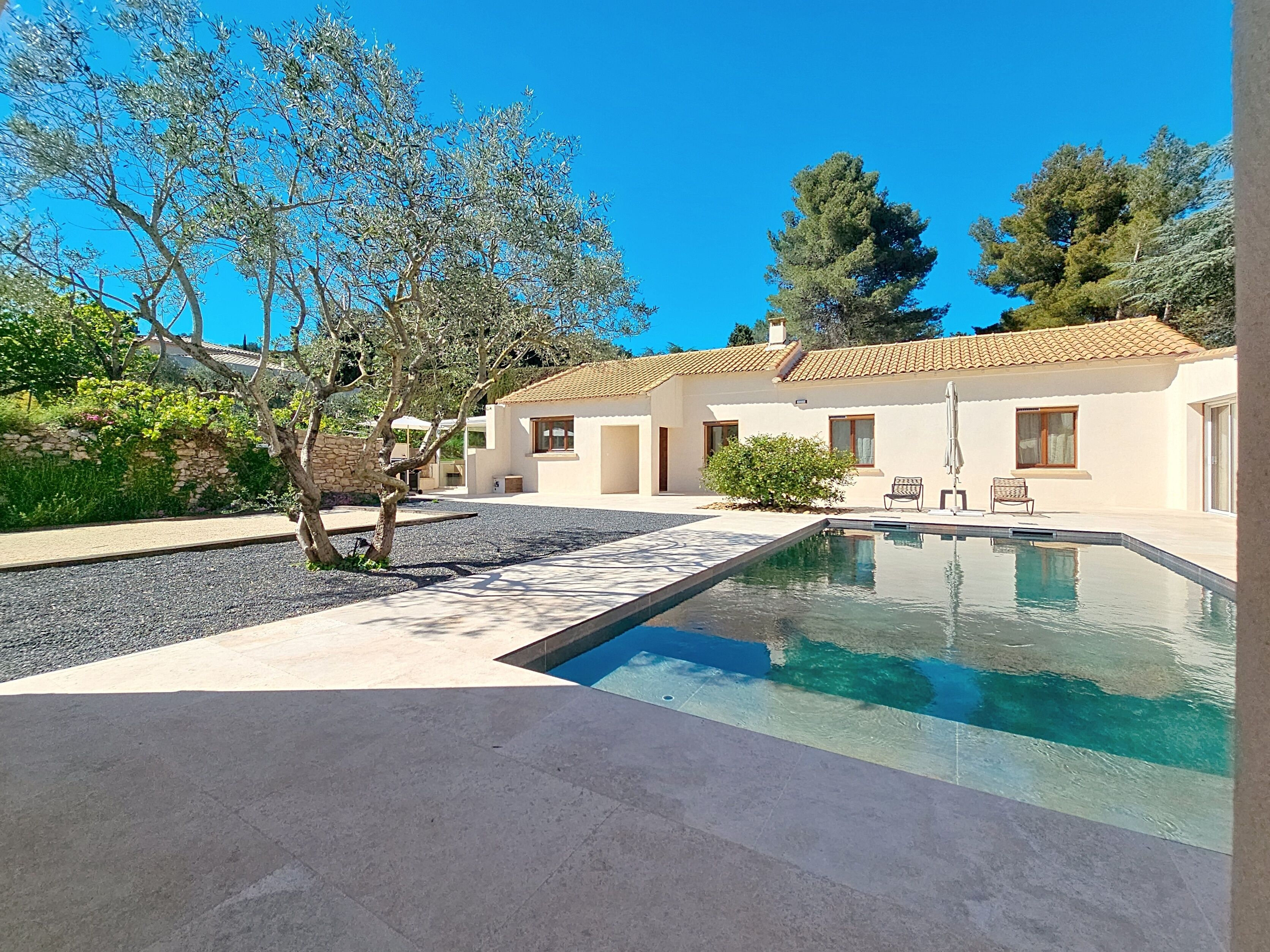 A modern house with a swimming pool, outdoor seating, and a stone wall.