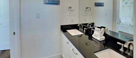 A modern bathroom with two sinks, a large mirror, and a towel rack.