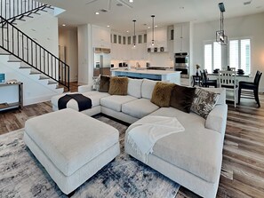 A modern living room with a sectional sofa, ottoman, and a staircase. - Seabreezy Lane by Ryson Vacation Rentals (Galveston)