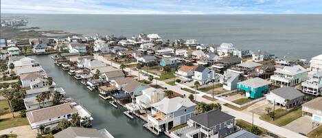 A coastal residential area with houses along a waterway, docks, and a clear view of the ocean.