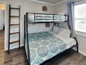 Un lit superposé avec une couvre-lit à motifs, une échelle en bois, un panier en osier et une fenêtre avec des rideaux.