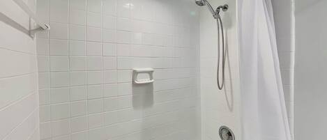 A bathroom with white tiled walls, a bathtub, a shower with a handheld showerhead, and a toilet.