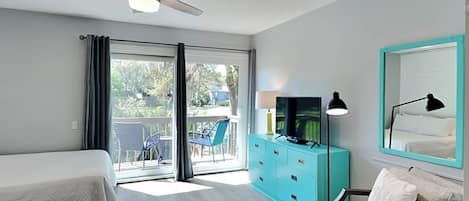 A hotel room with two beds, a teal dresser, a ceiling fan, and a balcony with chairs.