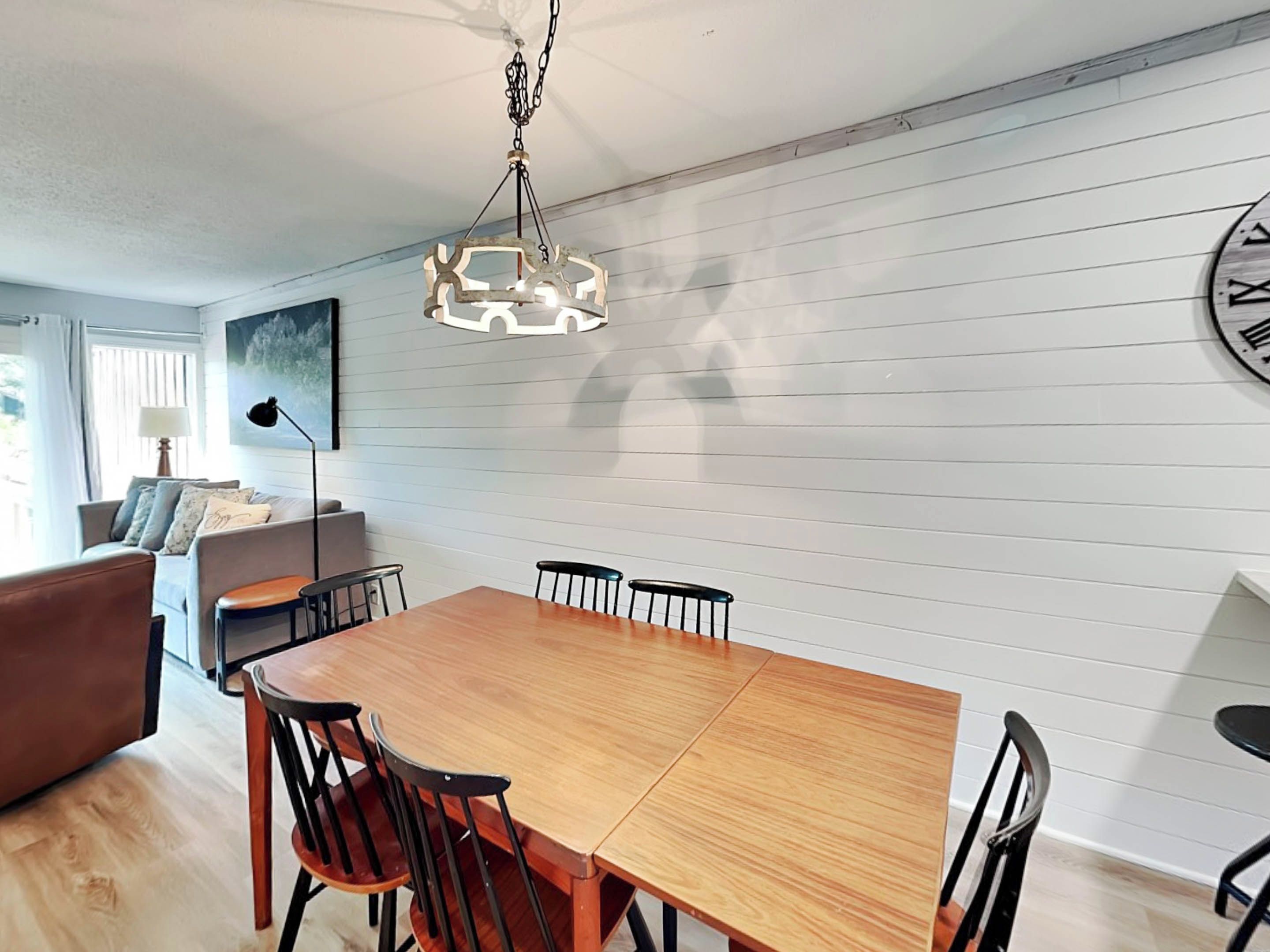 Un coin repas avec une table et des chaises en bois, un luminaire suspendu et une grande horloge murale.