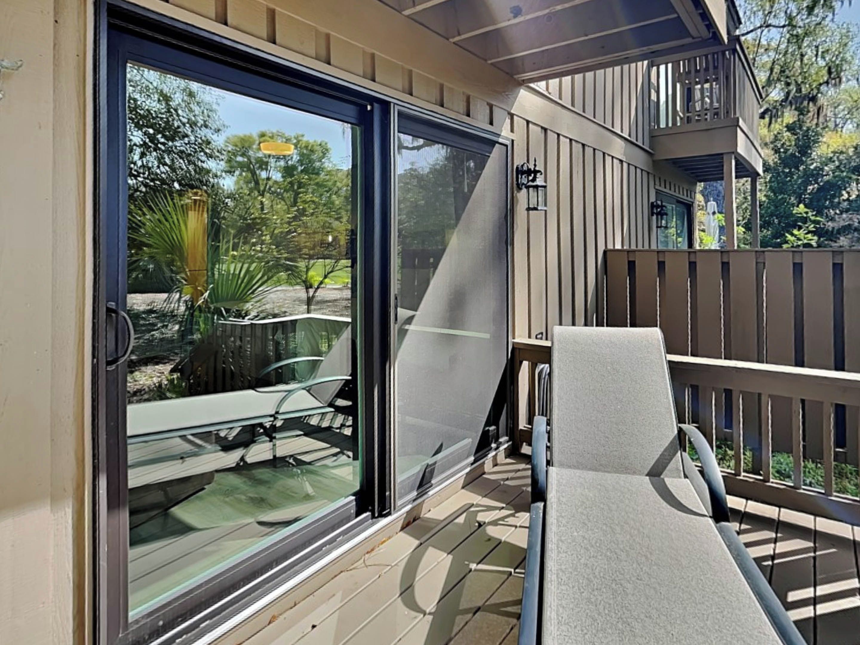 A covered outdoor area with a sliding glass door, a cushioned chair, and a wooden deck.