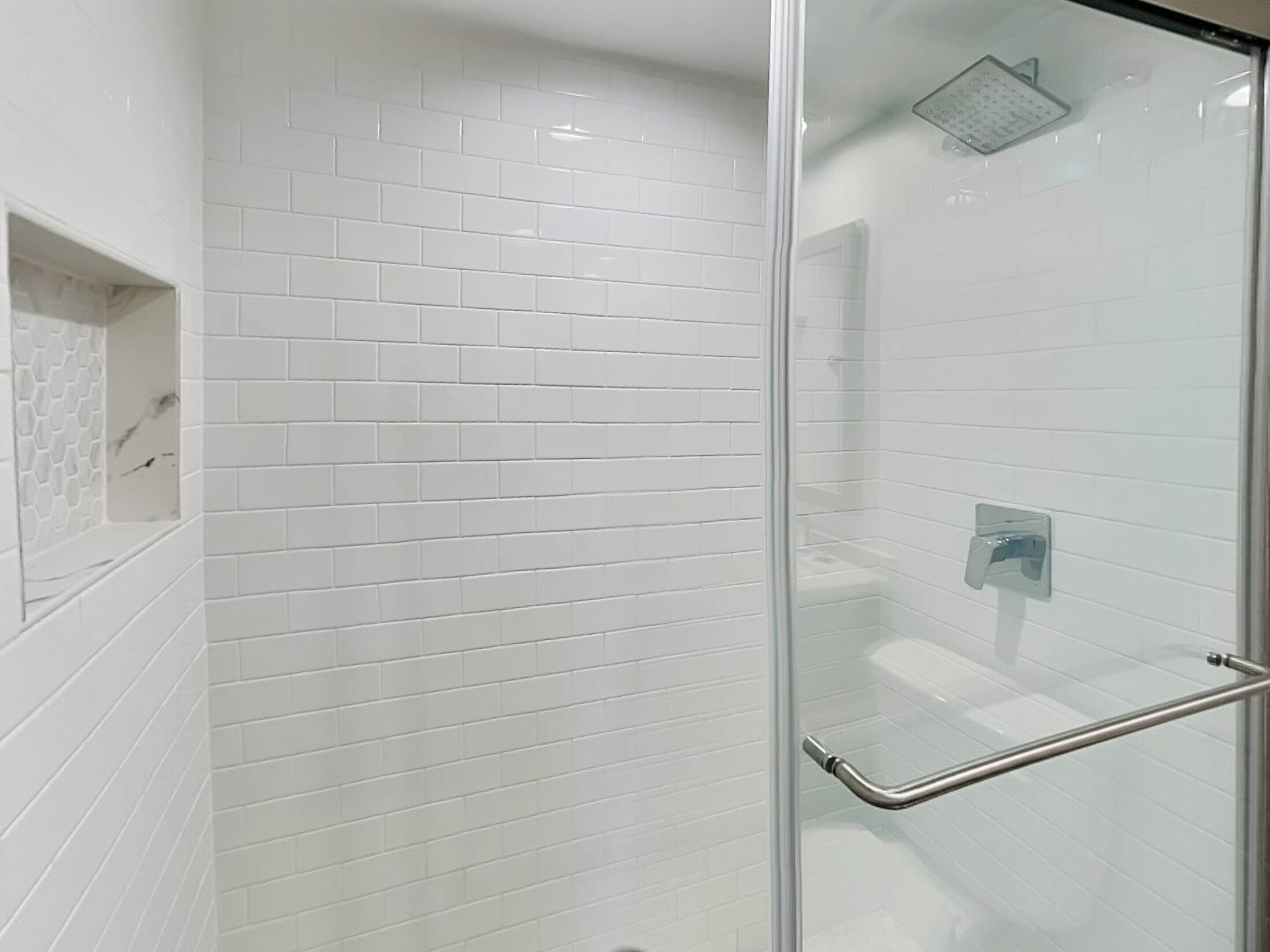 Een moderne badkamer met witte metro tegels, een glazen douchecabine en een metalen handgreep.