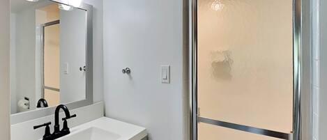 A bathroom with a white sink, black faucet, and a mirror above it. There is a shower with a glass door and a towel rack above it.