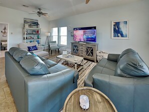 A modern living room with two grey sofas, a coffee table, a TV, and a bookshelf.