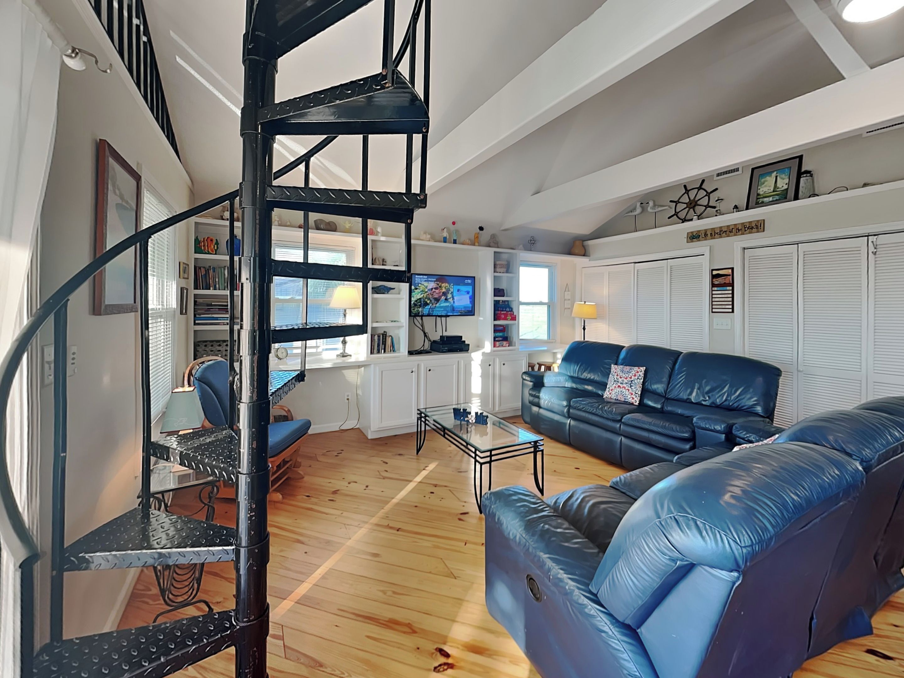A modern living room with a blue leather sofa, a black spiral staircase, and a TV on a white cabinet.