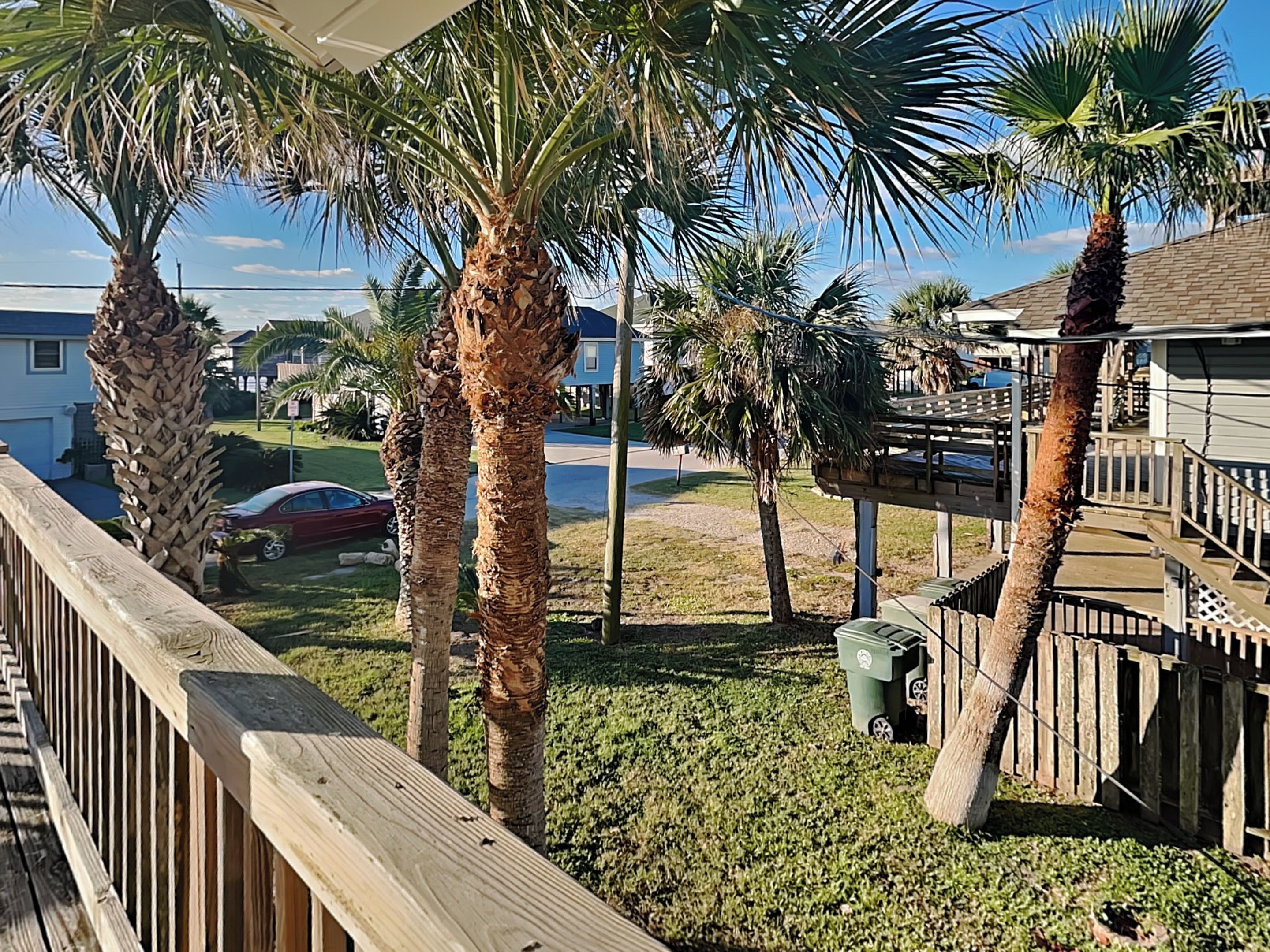 A residential area with palm trees, a wooden deck, and a house with a balcony.