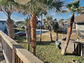 A residential area with palm trees, a wooden deck, and a house with a balcony. - Beach Oasis by Ryson Vacation Rentals (Galveston)