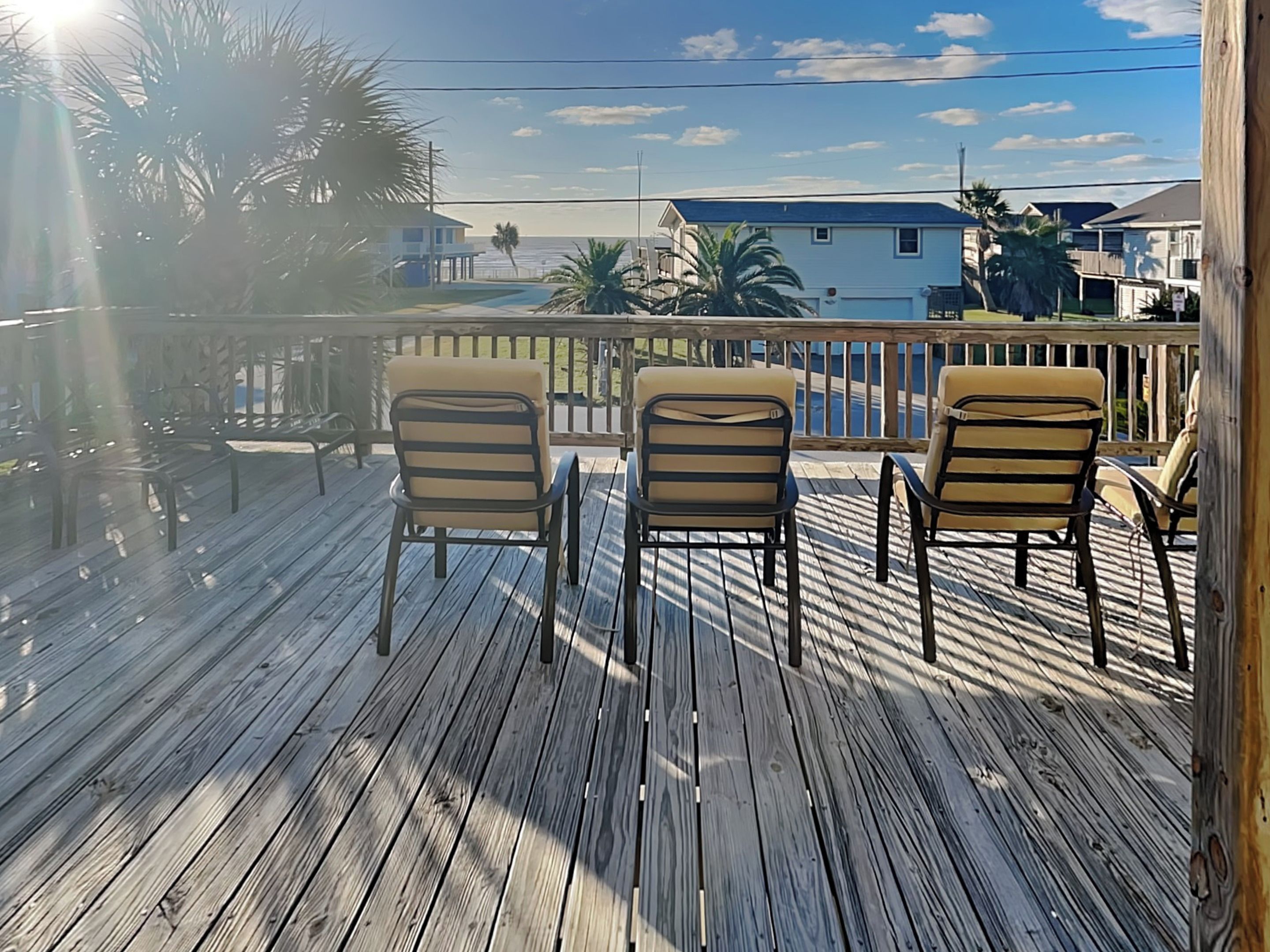 Une terrasse en bois avec deux chaises donnant sur une piscine et l’océan.