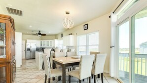 A spacious kitchen with a dining area, featuring a large window with blinds, a ceiling fan, and a modern chandelier.