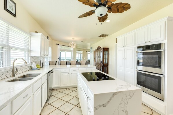 A spacious kitchen with white cabinetry, a central island, and built-in ovens.