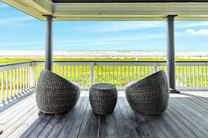 A covered outdoor area with three woven chairs facing a view of the beach.