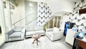 Una sala de estar moderna con una escalera, paredes con un diseño gris y blanco, y un televisor de pantalla plana sobre un mueble.