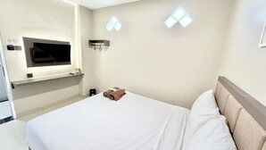 Habitación de hotel con cama, televisor montado en la pared y una pequeña estantería con un control remoto.
